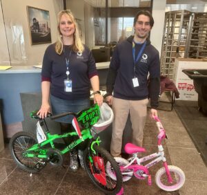 One man and one woman standing near children's bikes while smiling.