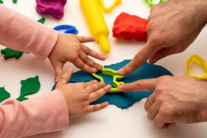 Close up of hand of young child playing dough with her father.
