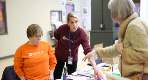 Photo of Summit DD team members Erin and Jessica showing a community member assistive technology options.