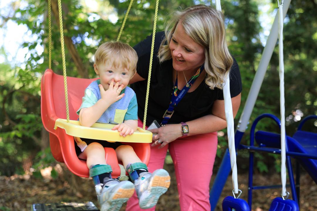 Joyful toddler in a safety swing with adult assisting
