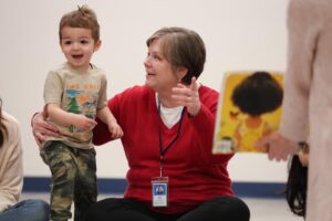 Smiling female Developmental Specialist sitting on the floor assisting a happy young boy with music therapy