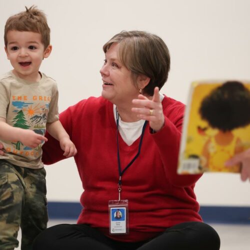 Smiling female Developmental Specialist sitting on the floor assisting a happy young boy with music therapy