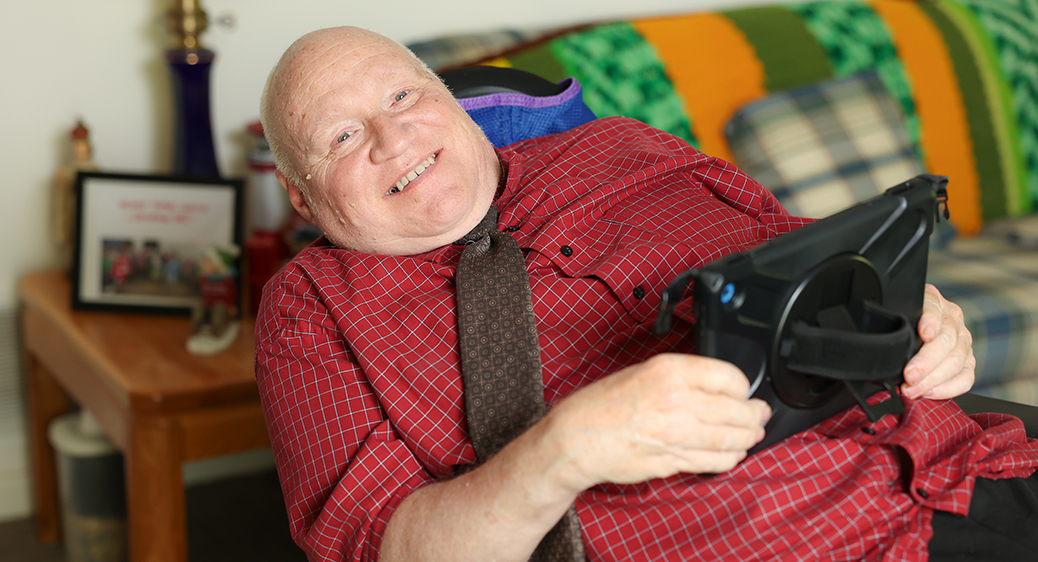 Older man smiling in his living room while using an iPad for remote tech monitoring services.