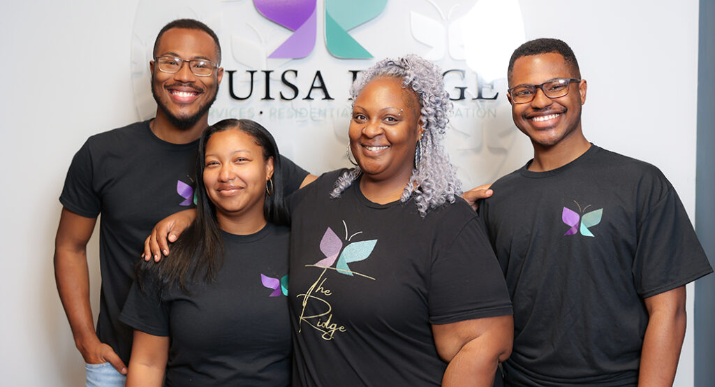 Group of people smiling in front of a sign that says Louisa Ridge, a local disability provider.