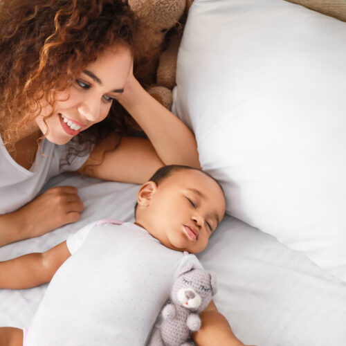 Young mom smiling next to her sleeping baby on a bed