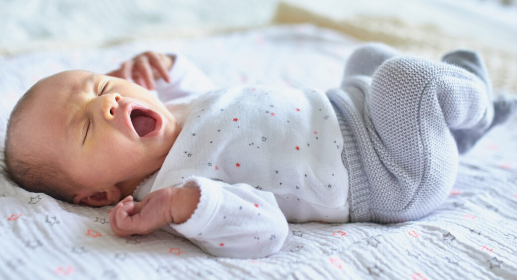 Newborn baby in onsie, pants and socks sleeping and yawning in crib