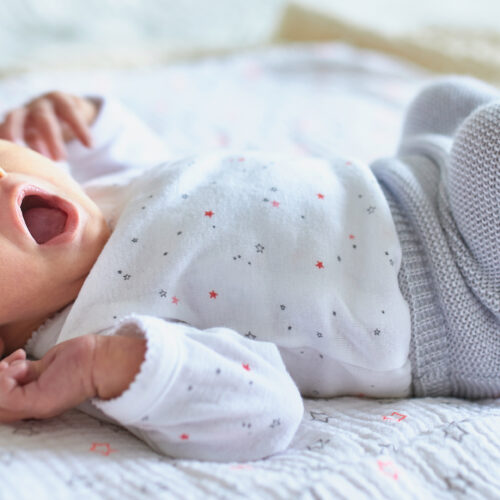 Newborn baby in onsie, pants and socks sleeping and yawning in crib