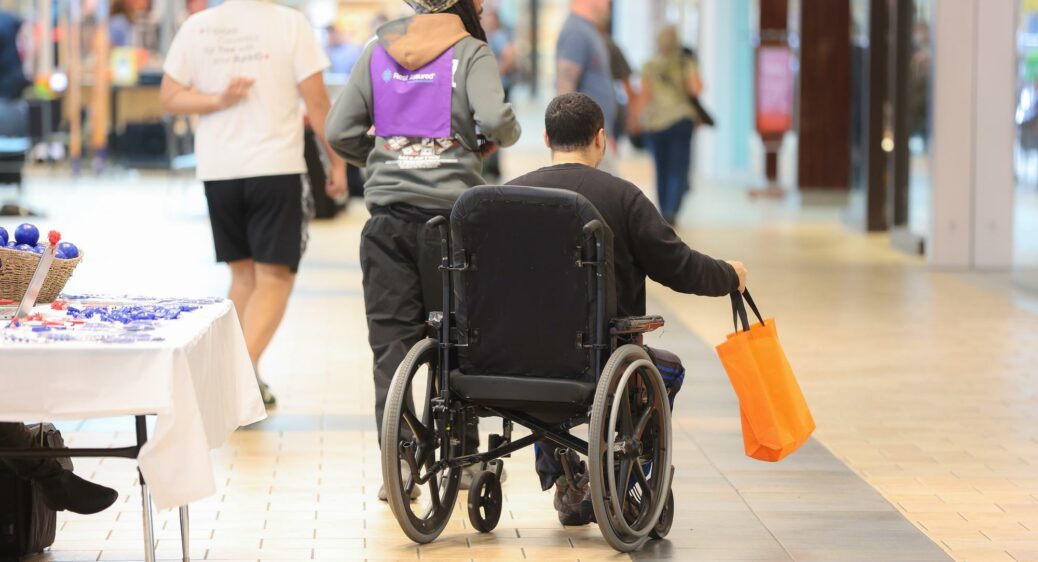 image of man in a wheelchair from behind holding an orange bag