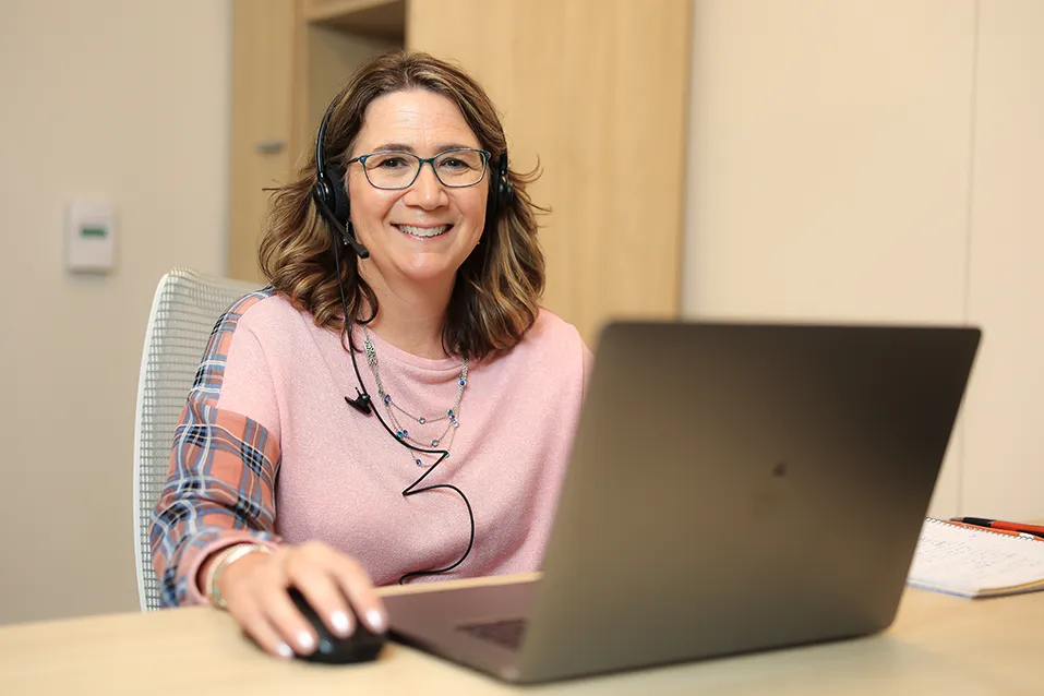Smiling woman wearing a call headset with laptop and mouse in front of her