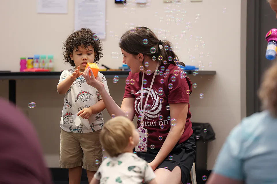 Young Summit DD female Developmental Specialist blowing bubbles with 2 young children