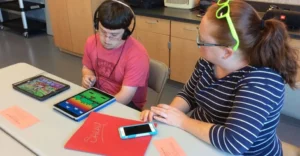 student using headphones and a tablet with instructor to his left