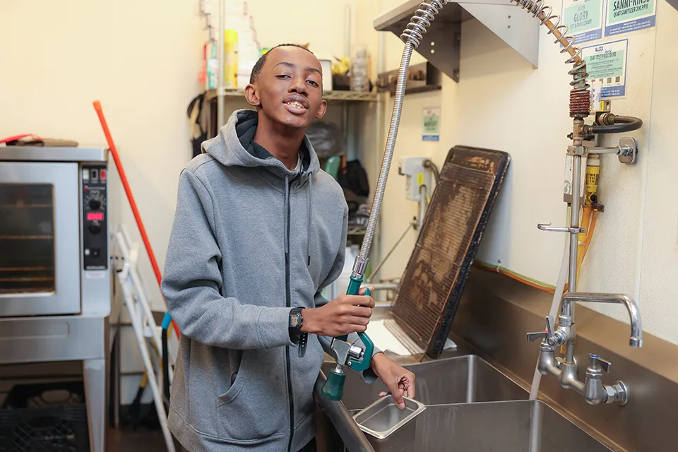 Teenager working in the kitchen of a business washing dishes