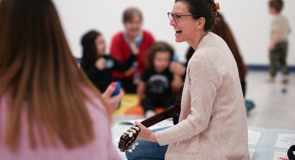 Female music therapist sitting on the floor singing and playing the ukulele during a session with children