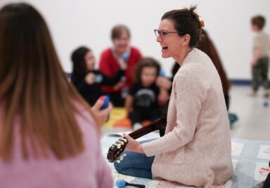 Female music therapist sitting on the floor singing and playing the ukulele during a session with children