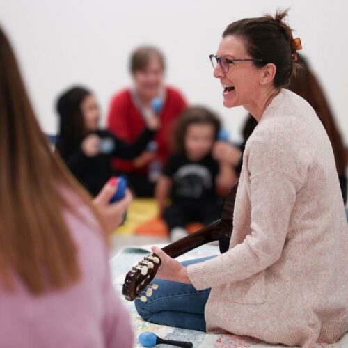 Female music therapist sitting on the floor singing and playing the ukulele during a session with children
