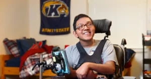 Young man in a wheelchair posing for a photo in his dorm room at KSU