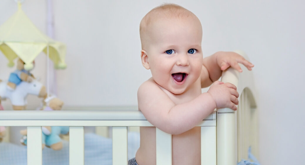 Smiling Caucasian baby boy standing in looking at camera.
