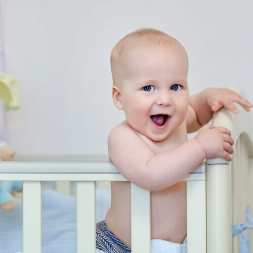 Smiling Caucasian baby boy standing in looking at camera.