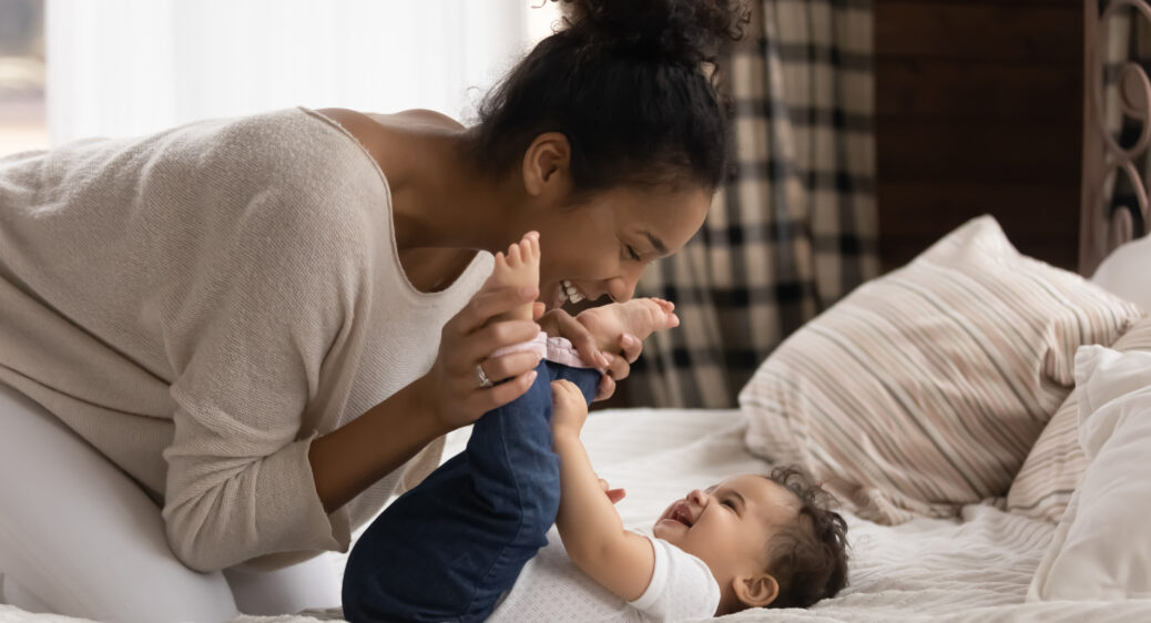 Smiling young mother playing with baby laying on a bed