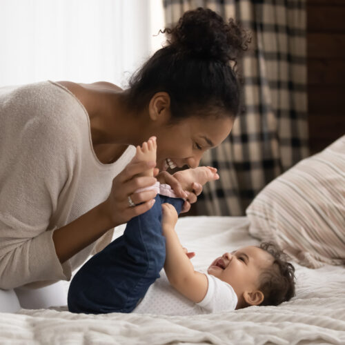 Smiling young mother playing with baby laying on a bed