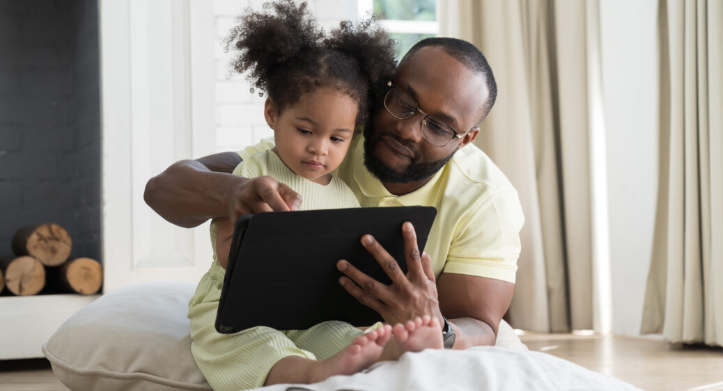 Father and baby daughter sitting together using digital tablet to learn or communicate