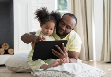Father and baby daughter sitting together using digital tablet to learn or communicate