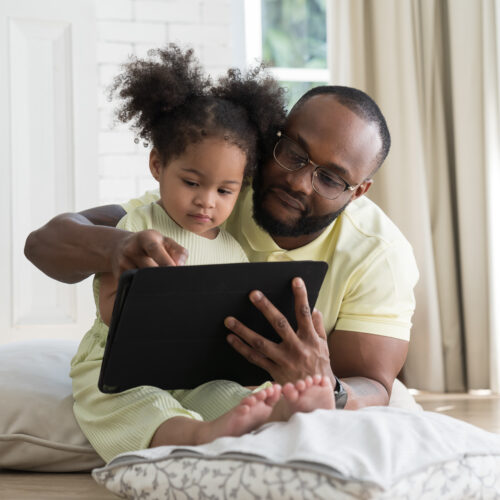Father and baby daughter sitting together using digital tablet to learn or communicate