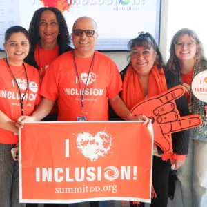 Group of 5 Summit DD employees all wearing orange and celebrating Summit DD's Inclusion Day holding a sign that says: I [heart] inclusion!