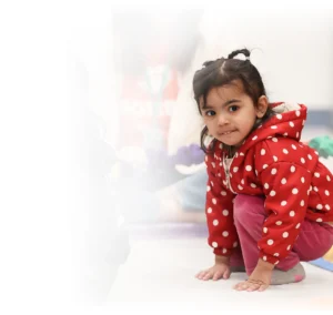 Little girl in red polka-dot coat crouched down looking at the camera