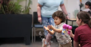 little boy with curls catching bubbles from a pink bubble gun toy