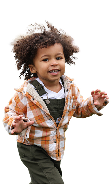 Child smiling while running with the wind blowing in his curly hair.