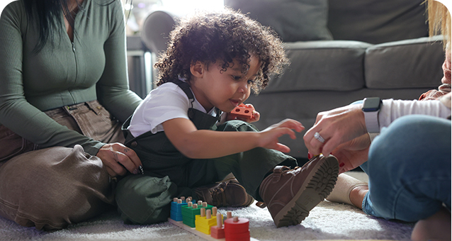 Child sitting on living room floor playing with blocks with the assistance of his mother and Summit DD Developmental Specialist.