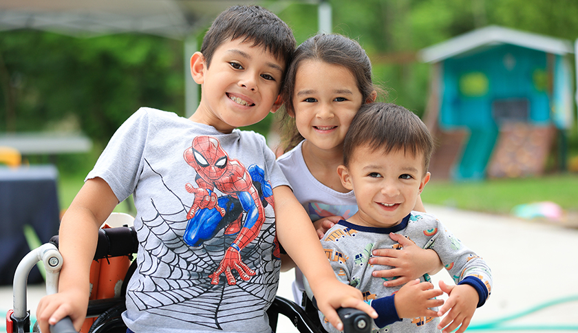 Three siblings smiling and embracing each other while playing in their backyard.
