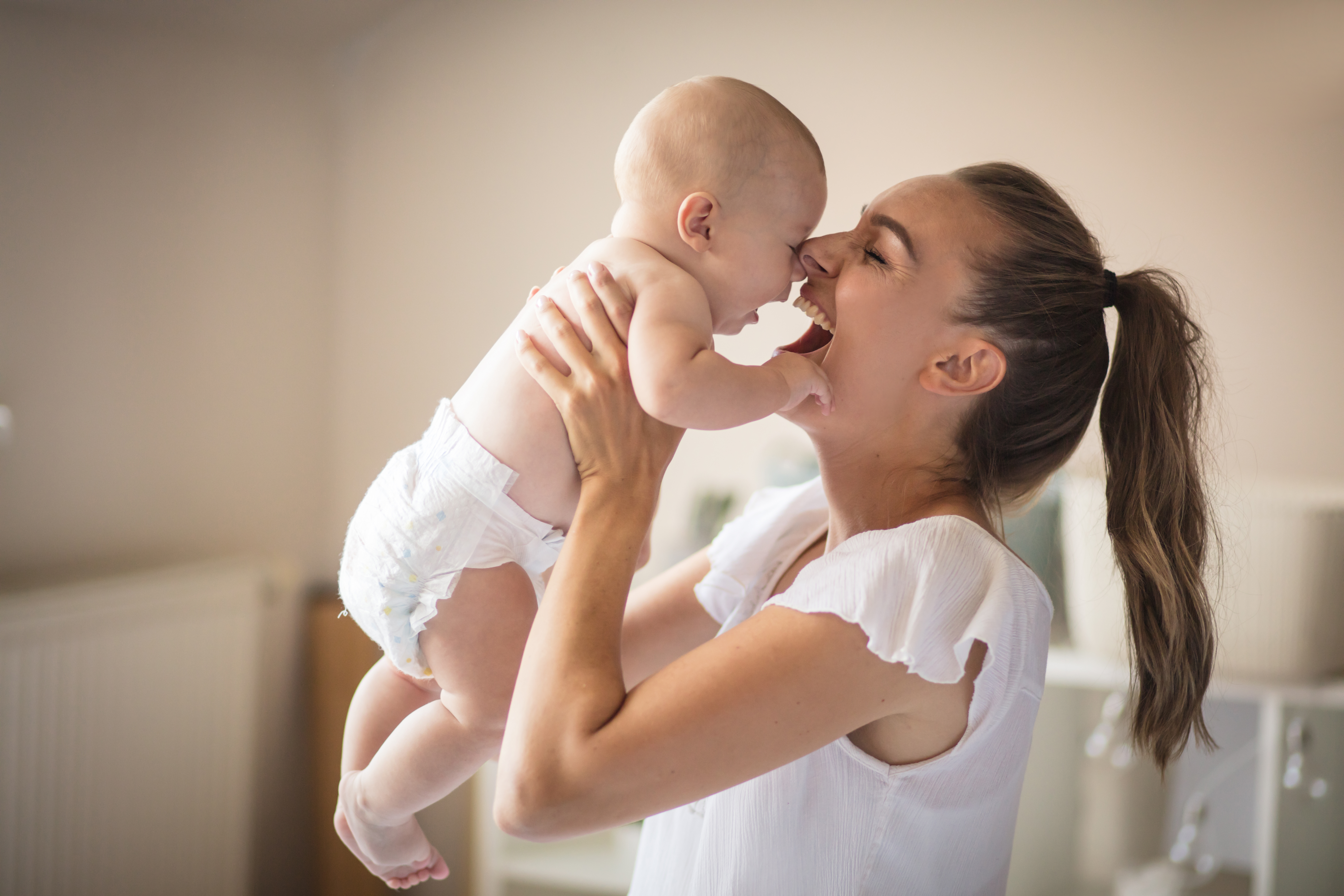 mom lifting up infant in diapers in playful manner