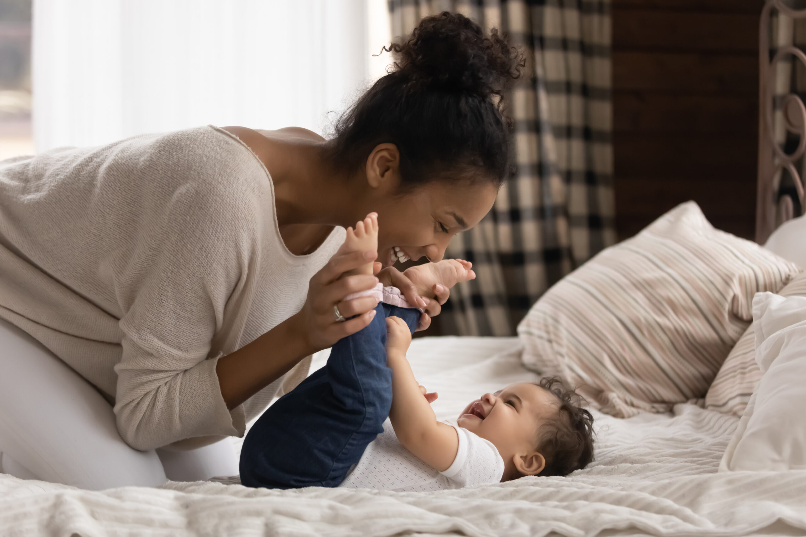 Smiling young mother playing with baby laying on a bed