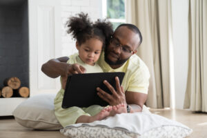 Father and baby daughter sitting together using digital tablet to learn or communicate