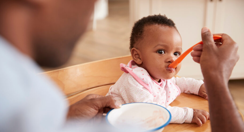 Baby in high chair being fed with a spoon by a parent