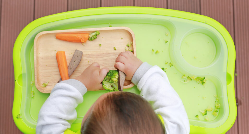 Overhead view of baby in highchair with vegetables on the tray