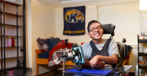Young man in a wheelchair posing for a photo in his dorm room at KSU.