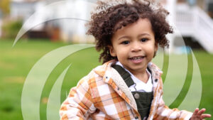 Young boy with bouncy curly hair running and laughing through his back yard.