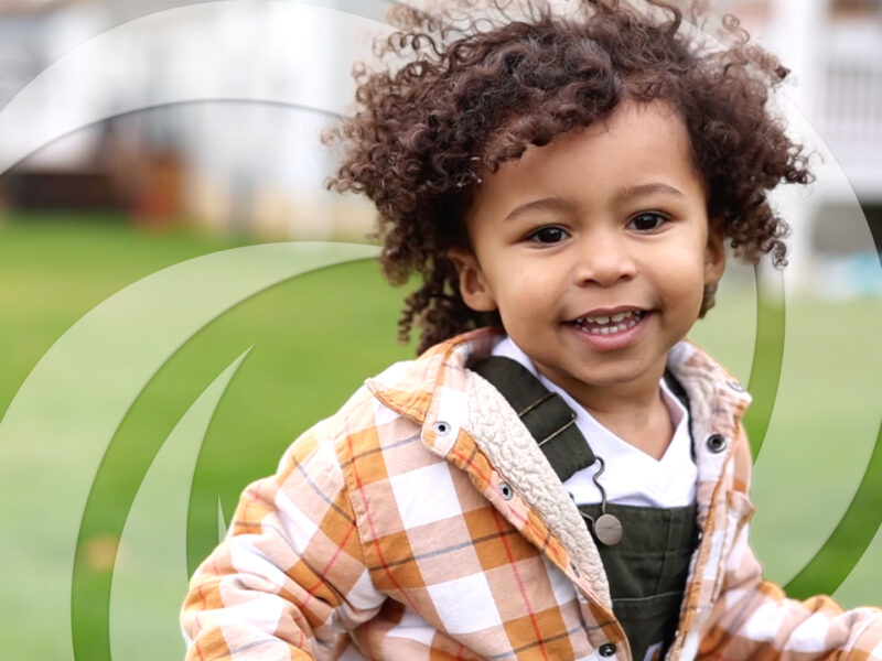Young boy with bouncy curly hair running and laughing through his back yard.