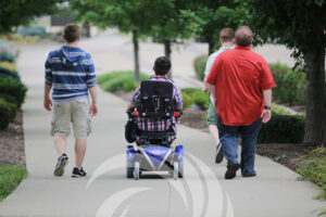 Group of four people, one in wheelchair, walking down a path with their back toward the camera. A white Summit DD swirl logo rises from the bottom of the image.