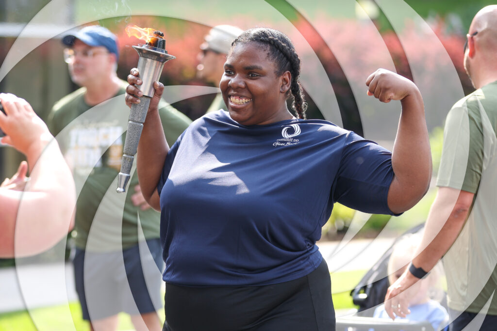 Smiling portrait of young woman holding the Special Olympics torch while flexing her arm showing her strength.