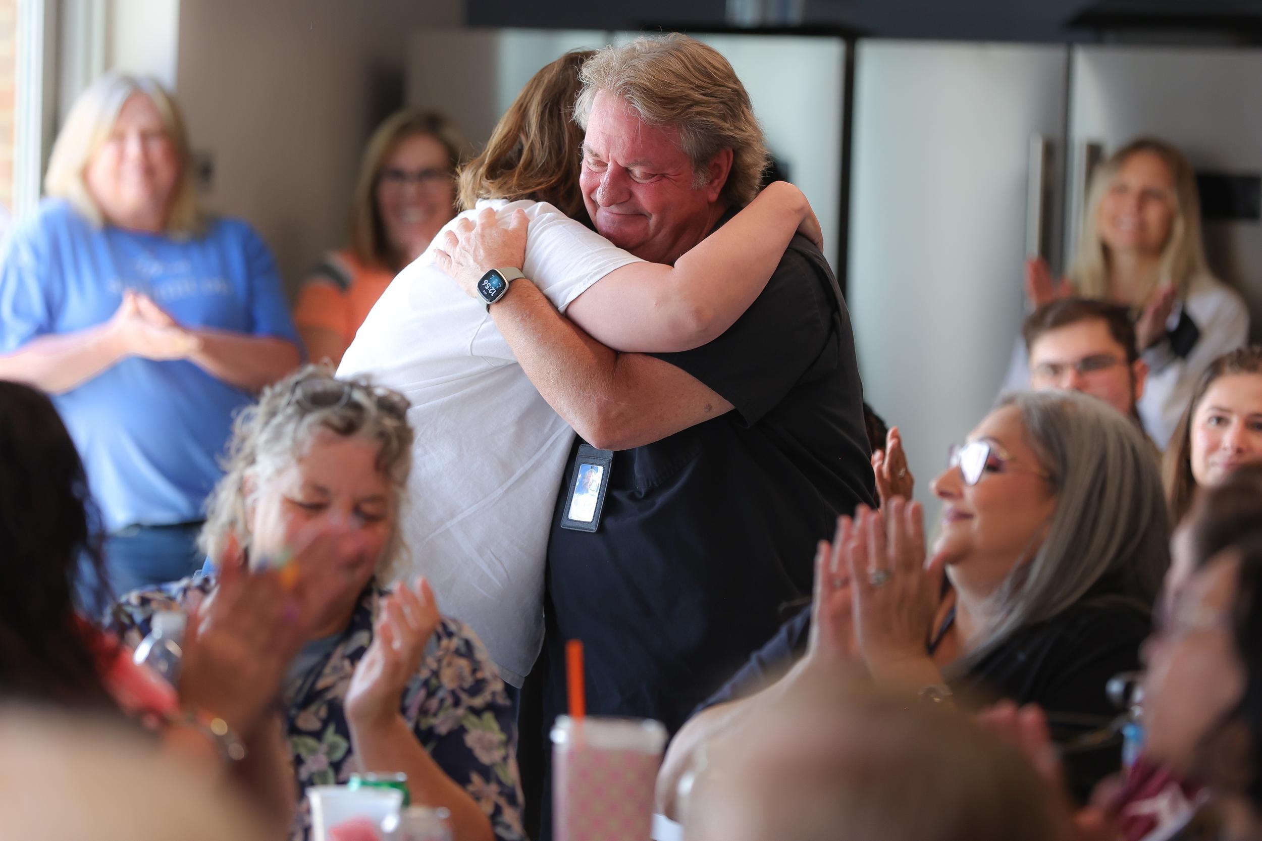 Two adults hugging with crowd clapping around them (decorative)