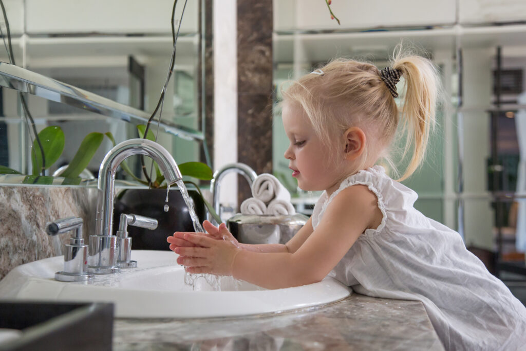 Profile picture of a toddler washing her hands in a bathroom sink by herself