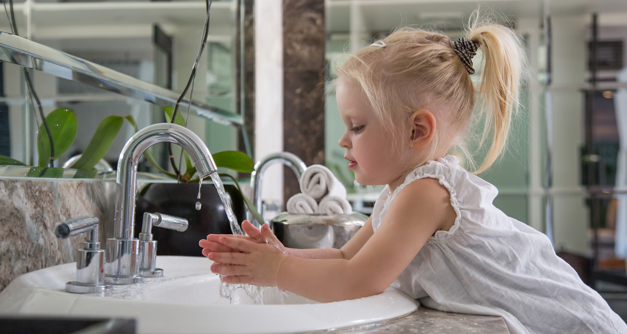 Profile picture of a toddler washing her hands in a bathroom sink by herself