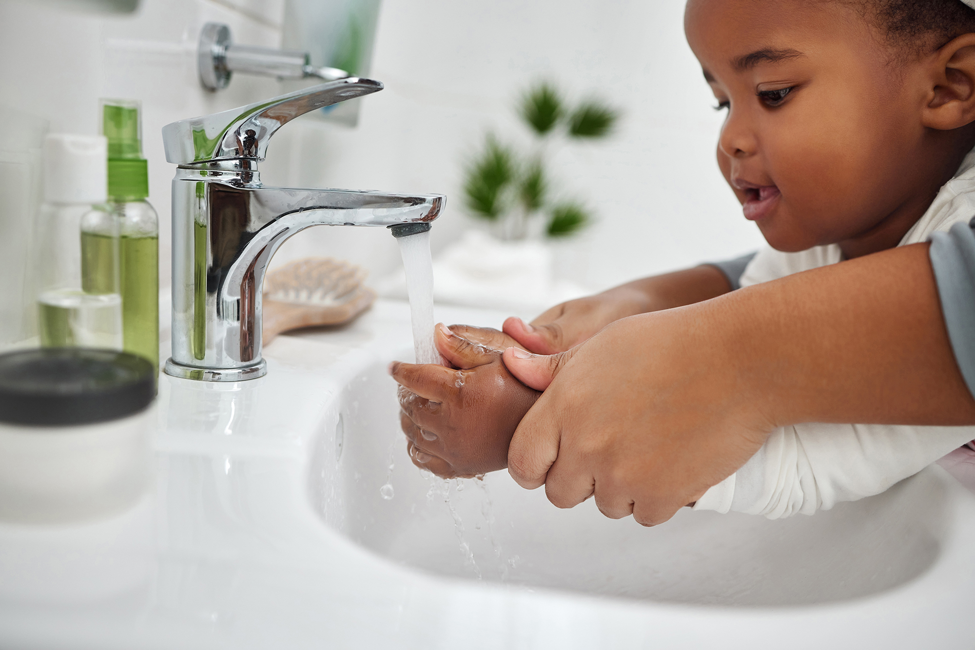 Close up of toddler washing hands in bathroom sink with the help of her mom