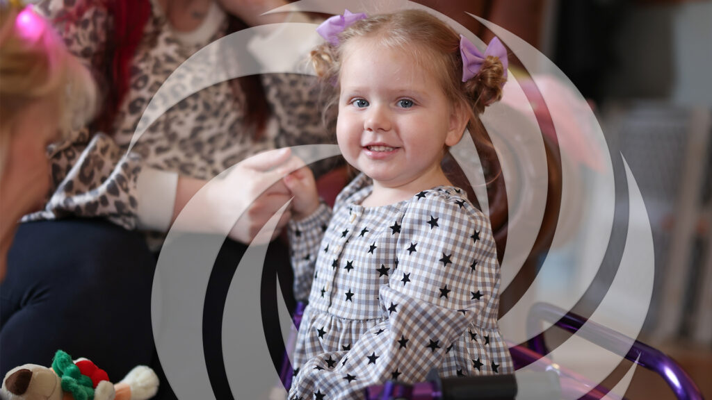 Portrait of young girl smiling while holding her mother's hand during a Summit DD Early Intervention home visit.