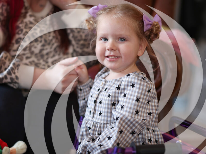 Portrait of young girl smiling while holding her mother's hand during a Summit DD Early Intervention home visit.