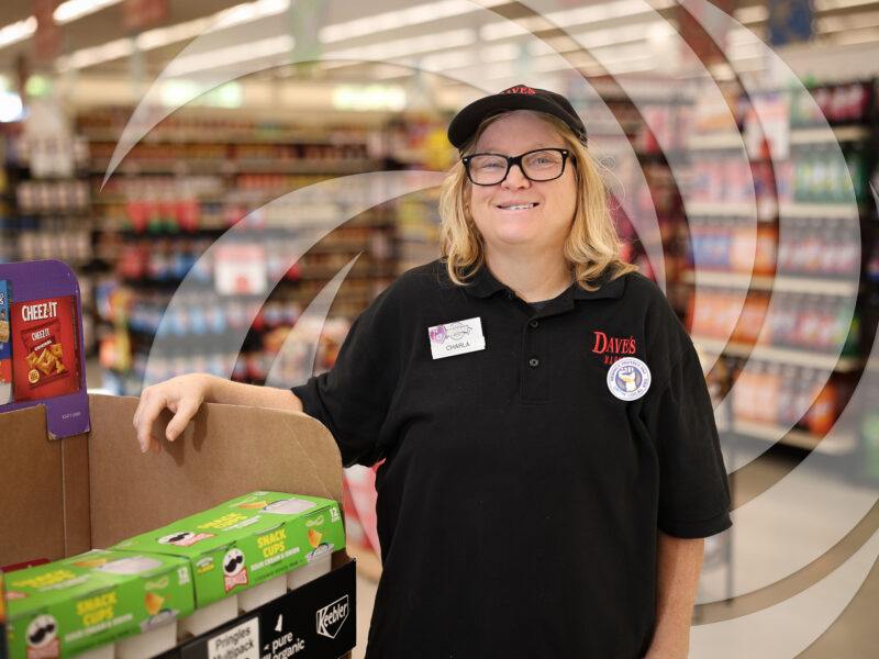 Smiling woman standing in a grocery store where she is employed.